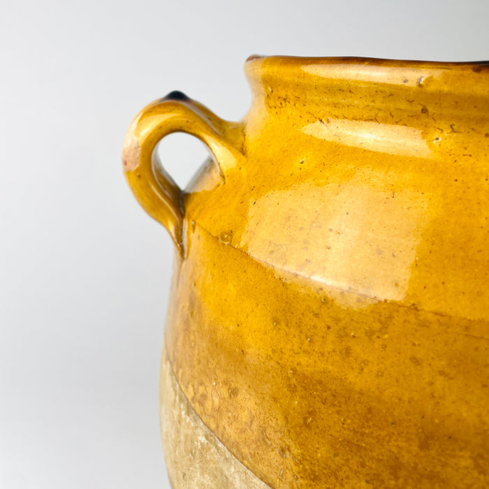 Twin handled French confit jar dating to the late 19th century, with a rounded terracotta body, thick flared lip and amber yellow glaze across the shoulder. Tonal variations, small firing marks and glaze pooling distinguish the hand thrown pottery as a Mediterranean decor accent.
