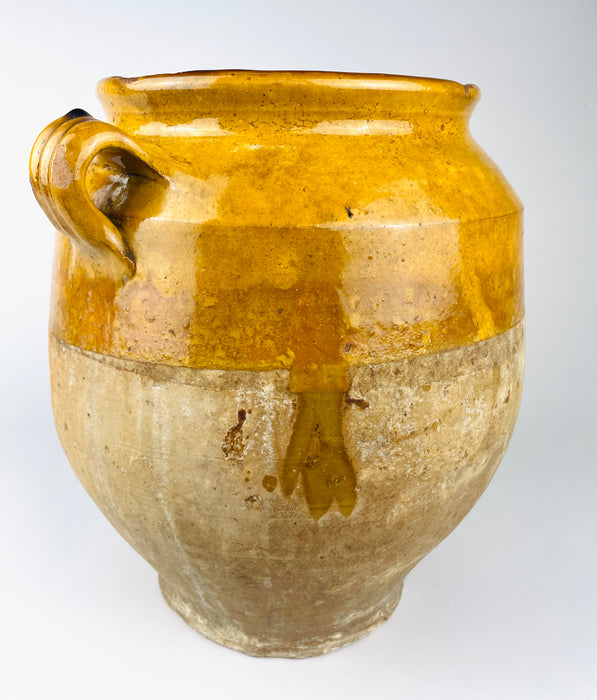 late 19th century French terracotta confit jar with a bulbous body, flared rim and two small ear handles. Honey and ochre glaze covers the shoulder while the lower clay remains matte and weathered, giving this functional food preserving pot strong rustic home decor character.