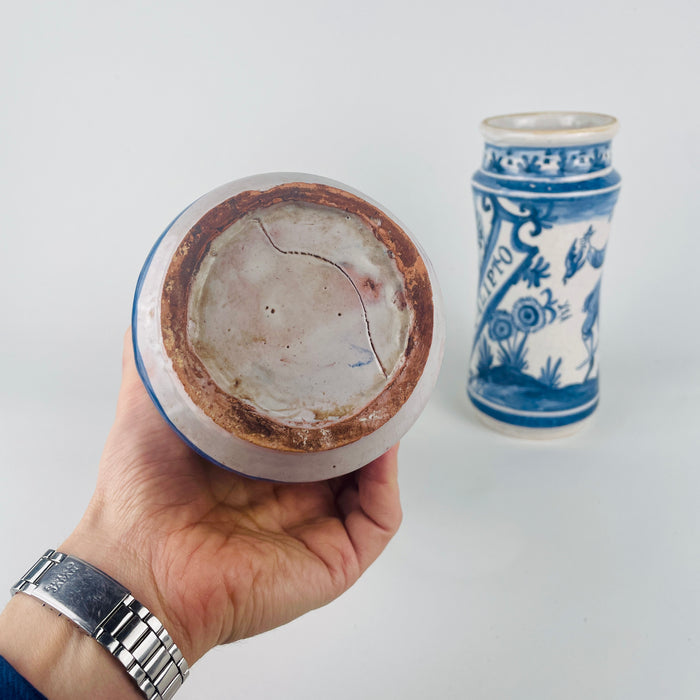 Hand holding a ceramic pot with a damaged interior, next to another ceramic pot with blue and white design on a light gray background.