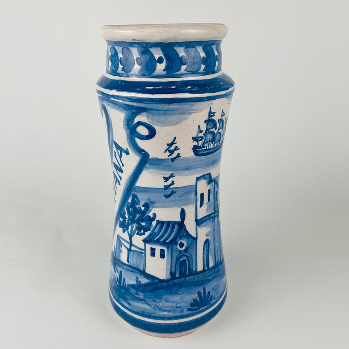 Spanish blue and white faience botamen jars, albarello type, with hand painted borders and central banners for medicinal ingredients. The set mixes a galleon ship scene and a figure scene, giving strong traditional Spanish pottery character. Works as kitchen counter utensil holders, bathroom cotton storage, or shelf decor in farmhouse decor and rustic home decor spaces, with visible age wear and glaze crazing typical of tin glazed ceramics.