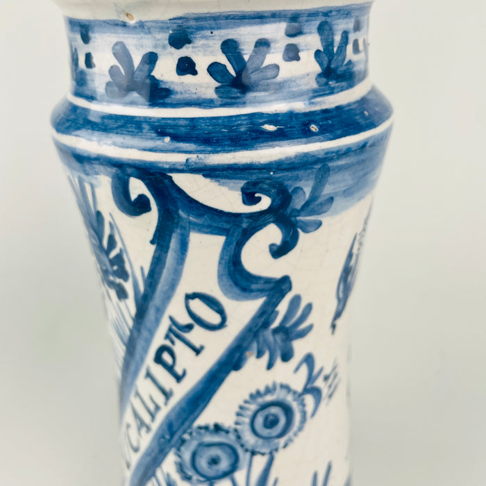 Collectible Spanish faience apothecary jar pair with cobalt blue decoration, botanical inscriptions, and traditional albarello silhouettes. The white tin glazed ceramic surfaces show age related crazing and small wear, adding texture for wabi sabi decor and rustic home decor. Display together as Mediterranean decor accents, or separate them as kitchen utensil crocks