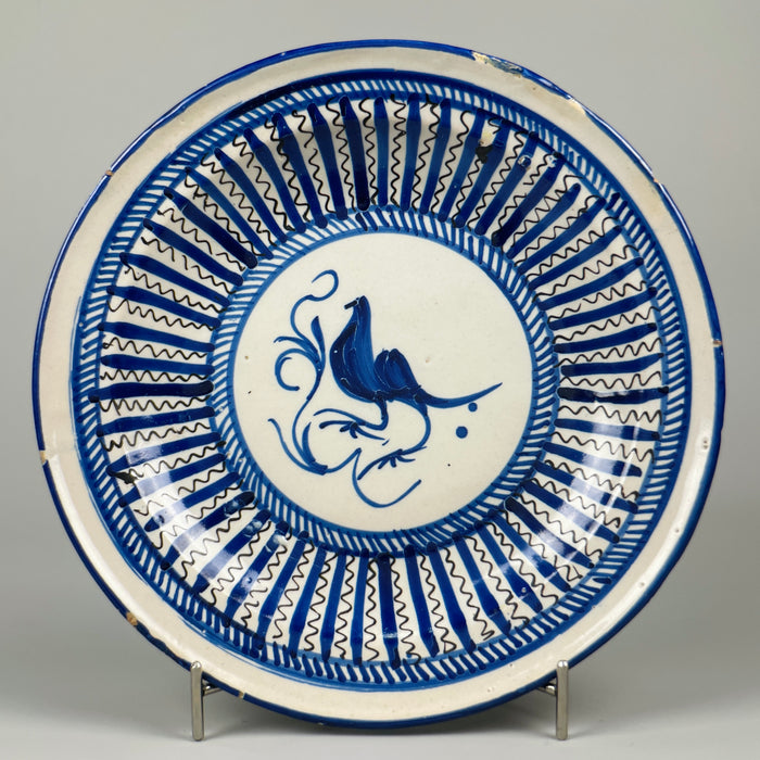 Antique Spanish Manises plate, cobalt blue bird with concentric zigzag and stripe patterns, hand-painted on tin-glazed ceramic, shown front-on for decorative wall use in rustic or Mediterranean interiors.
