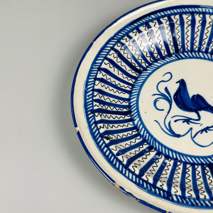 Cobalt blue decorative bird plate from late 19th-century Spain, crafted in Manises using tin-glazed ceramic techniques, with central avian figure and surrounding zigzag brushwork for wall decor.