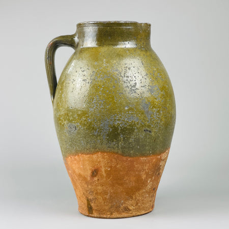 Antique Spanish terracotta pitcher from 19th century Toledo, photographed from the front to show olive-green glazed upper body, red clay base, sculptural proportions, and rustic form suited to farmhouse or Mediterranean interior decor.