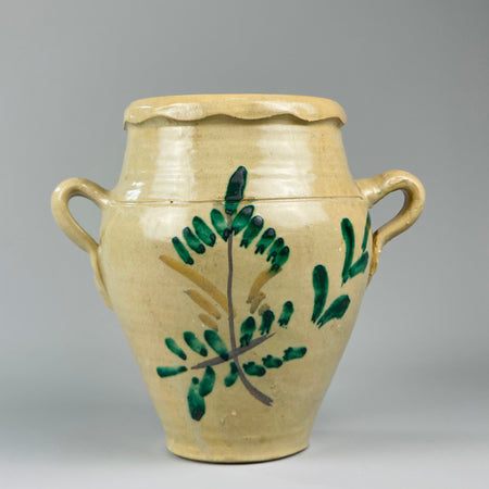 Early 20th-century Spanish Lucena orza jar with cream glaze and hand-painted green plant motifs, featuring dual side handles and a scalloped rim, traditionally used for food storage in Andalusian kitchens and Mediterranean rustic interiors.
