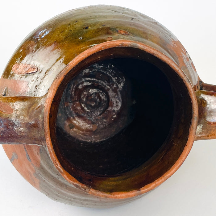 Spanish glazed terracotta vase, with visible hand shaping, darkened wear and areas where the brown glaze reveals the red clay beneath. The two handled nineteenth century pottery jar has a practical storage form and a sculptural presence suited to farmhouse decor, wabi sabi decor and antique pottery collections.