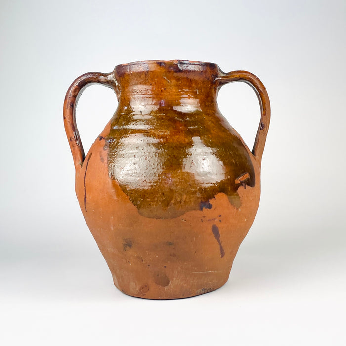 Wheel thrown Spanish terracotta vase displaying horizontal turning lines beneath the amber brown glaze and subtle hand formed irregularities throughout the body. The two handled Castilian orza jar dates to the nineteenth century and combines utilitarian pottery construction with an expressive aged surface for antique and vintage home decor.