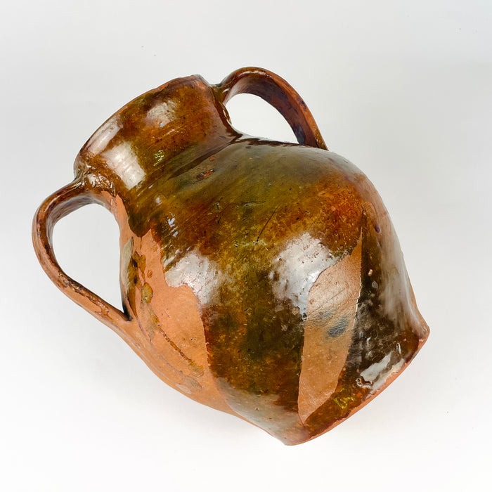 Antique Spanish glazed terracotta jar, where broad areas of unglazed orange red clay contrast with glossy honey and olive brown glaze. The visible wear, drips and handmade texture emphasize the nineteenth century orza vessel’s rural character and make it compatible with Mediterranean decor and farmhouse decor.
