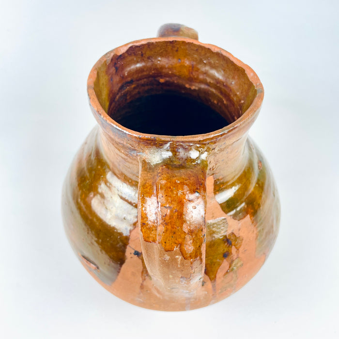 Antique Spanish pottery vase with a bulbous body tapering to a flat circular base, a short open neck and two high loop handles. The partially glazed terracotta surface combines amber, olive brown and warm red clay, creating a distinctive Castilian orza jar for a console, shelf or dining room centerpiece in Mediterranean decor.