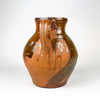 Large scale reference showing the antique Spanish terracotta vase held securely by an adult, clarifying its substantial rounded form and two tall handles. The nineteenth century Castilian orza jar has a glossy brown upper glaze, exposed red clay lower body and strong visual presence for farmhouse decor or rustic home decor.