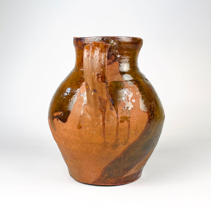 Large scale reference showing the antique Spanish terracotta vase held securely by an adult, clarifying its substantial rounded form and two tall handles. The nineteenth century Castilian orza jar has a glossy brown upper glaze, exposed red clay lower body and strong visual presence for farmhouse decor or rustic home decor.