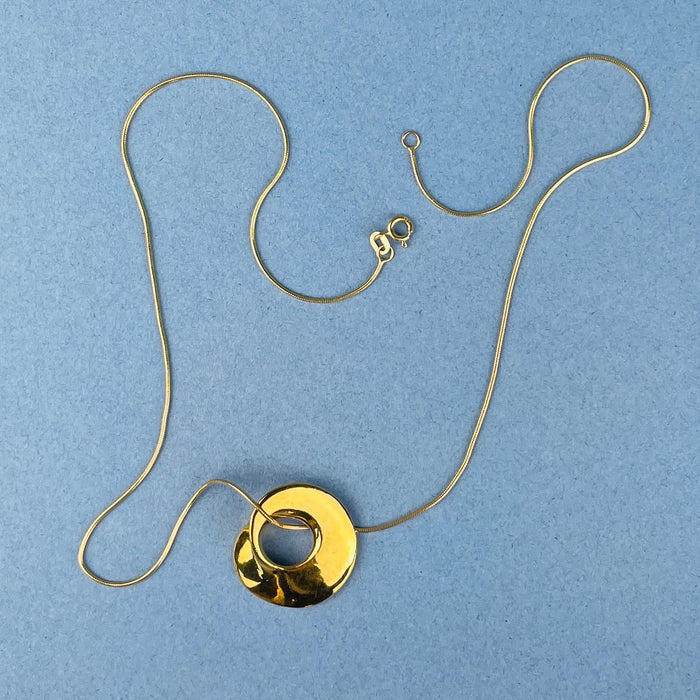 Wearable sculpture pendant with organic curves and a central cut-out, plated in 14k gold over bronze. Each piece is hand-carved in wax, cast in bronze, and finished as contemporary art jewelry. Designed for collectors who value sculptural jewelry and artisan design.