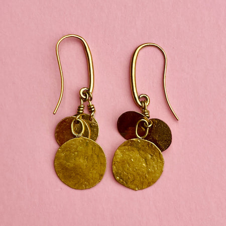 Pair of hammered disc drop earrings with reflective golden surfaces catching the light. Their handcrafted finish and comfortable nickel-free hooks make them suitable as everyday earrings, minimalist. Ideal for summer jewelry styling, minimalist wardrobes, and Mediterranean-inspired accessories. 