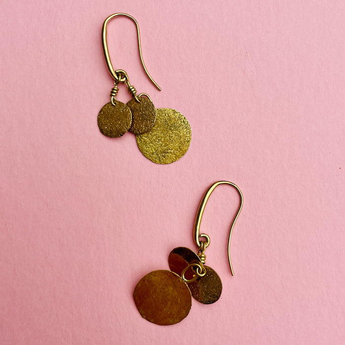 Detailed close-up of hammered gold-tone earrings featuring three discs in graduated sizes per earring. Their handmade, artisanal finish highlights Aurelia Collection craftsmanship. Perfect as statement dangle earrings, they complement minimalist styling, summer jewelry trends, and casual Mediterranean-inspired looks.
