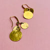 Pair of hammered coin drop earrings shown with reflective light on textured surfaces. Gold-tone alloy discs shimmer against nickel-free hooks, highlighting their versatile styling for resort fashion, capsule jewelry collections, or everyday lightweight wear with Mediterranean design influence.