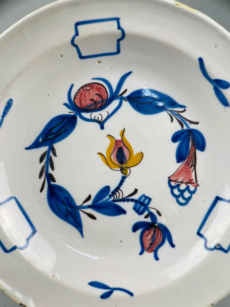Close-up of central floral motif on antique Manises plate showing detail of yellow flower with cobalt blue leaves and red accents, emphasizing artisanal brushwork and aged glaze.