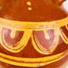 Antique water jug in terracotta from northern Spain, early 20th century, with a practical dual opening structure and hand applied handle joining the two necks across the top. The glossy upper surface is decorated with yellow painted arches and linear borders over a chestnut glaze, while the lower body shows matte raw clay with wear from age and handling. This Spanish botijo works as a table centerpiece, shelf accent, or pottery vessel in Mediterranean decor and vintage home decor.