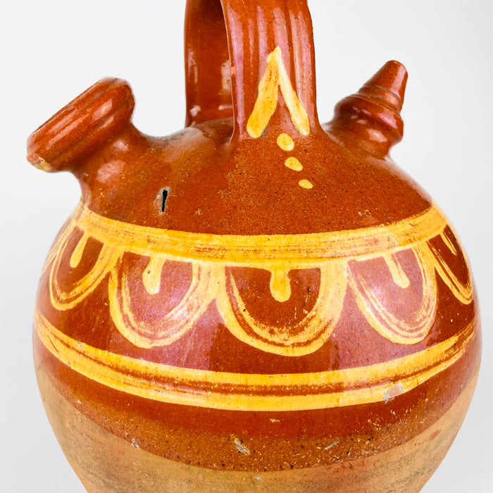 Hand painted glazed Spanish botijo in terracotta with a rounded body and narrow base, made for cooling water through porous clay construction. 
 The lower portion remains unglazed and timeworn, emphasizing its utilitarian history. This antique water jug fits farmhouse decor, rustic home decor, and antique pottery collections focused on Spanish ceramic.