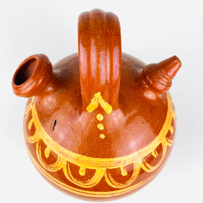 Hand painted glazed Spanish botijo in terracotta with a rounded body and narrow base, made for cooling water through porous clay construction. 
 The lower portion remains unglazed and timeworn, emphasizing its utilitarian history. This antique water jug fits farmhouse decor, rustic home decor, and antique pottery collections focused on Spanish ceramic.