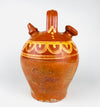 Northern Spain antique botijo in red clay, early 20th century, with a rounded shoulder, tapered body, and attached vertical handle spanning the top of the vessel. The upper body is glazed and painted in a yellow on brown palette, while the lower body remains unglazed and visibly worn, showing the honest surface of traditional utility pottery. This Spanish terracotta water jug is well suited to rustic decor, country pottery displays.