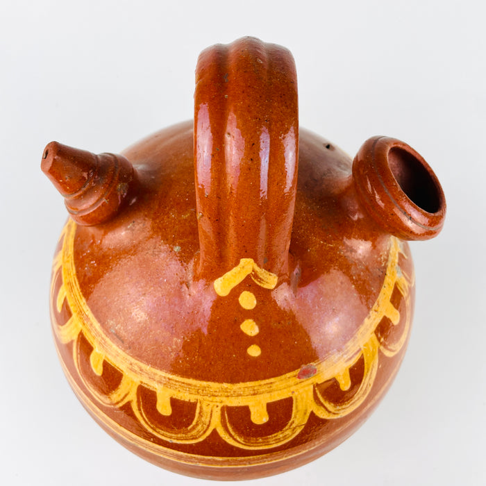 Antique terracotta water jug from Spain with hand painted folk decoration and a classic two opening botijo design. The larger mouth was intended for filling, the smaller spout for pouring or drinking, and the porous clay body helped keep water cool. The decorative shoulder band is painted in yellow over glossy brown glaze, while the lower half retains its raw terracotta finish. This northern Spanish ceramic vessel works naturally in Mediterranean decor, farmhouse decor, and vintage home decor.