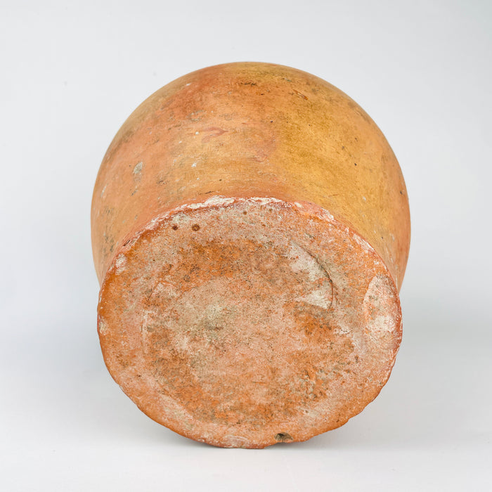 Spanish botijo water jug in antique terracotta, likely made for everyday domestic use in northern Spain during the early 20th century. The vessel combines a utilitarian form with restrained painted ornament, including yellow scalloped arches, linear bands, and a simple motif under the handle. The raw clay lower body, worn base, and glaze variation support its age and handmade character. This pottery jug can be used as a decorative vessel for shelves, consoles, and rustic home decor