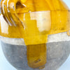 Detail of the antique French confit pot showing an applied terracotta loop handle, glossy ochre yellow glaze and a broad vertical glaze run extending onto the unglazed lower body. Fine crazing, worn edges and small exposed clay areas are clearly visible, emphasizing the hand-finished surface and genuine age of this 19th century French pottery vessel.