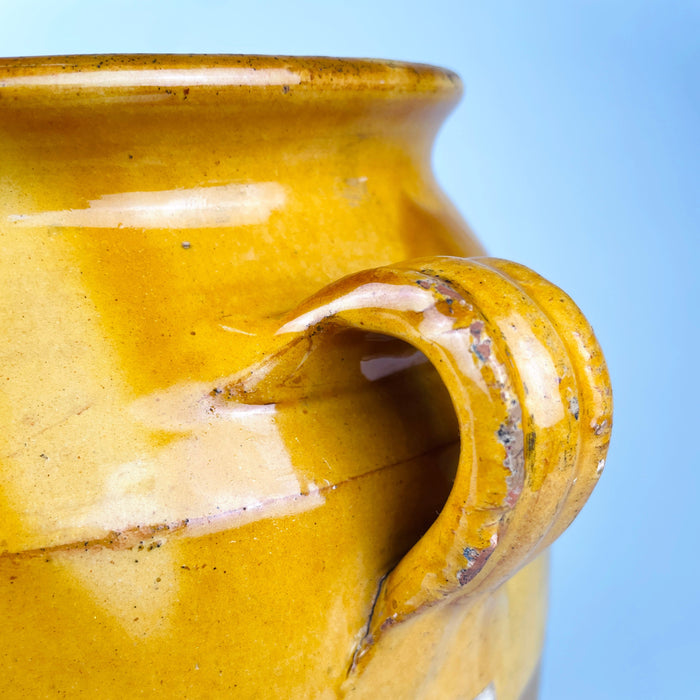Nineteenth century French confit pot showing mustard yellow glaze running unevenly over the shoulder and forming natural drips onto the raw terracotta lower body. Both applied loop handles remain intact, while glaze losses, rubbing and exposed clay document generations of use on this antique pottery jar suited to rustic home decor and wabi sabi decor.