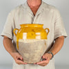Antique 19th century French confit pot in terracotta, with a rich ochre yellow glaze covering the rounded shoulder, flared rim, interior and two applied loop handles. The lower half remains unglazed, revealing a chalky timeworn clay surface with natural abrasion, glaze drips and losses that suit French country decor and farmhouse decor.