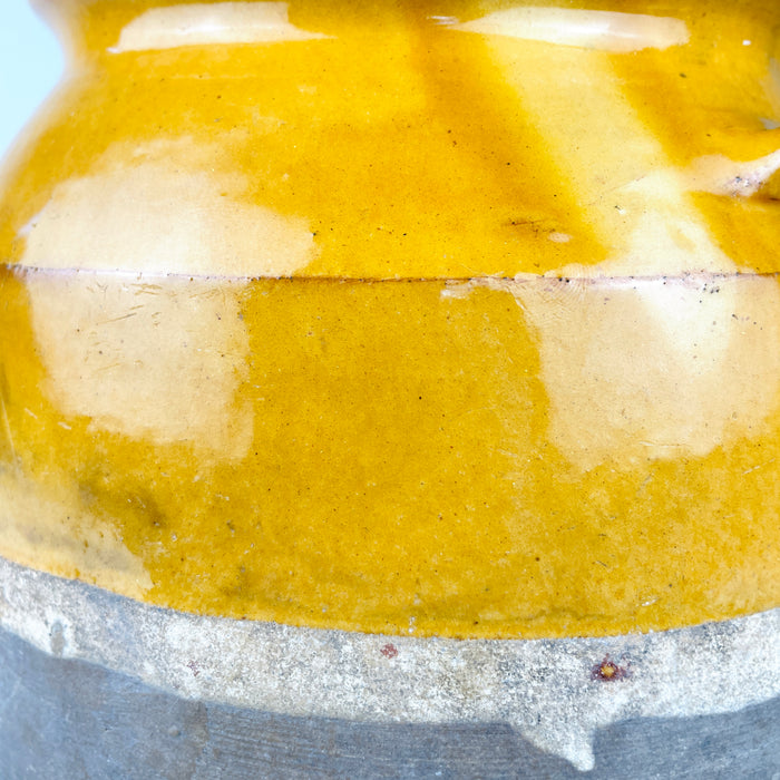 19th century French confit pot, showing the warm yellow glazed surface, circular throwing marks at the base and extensive age-related glaze wear with areas of exposed terracotta. The wide rolled rim also carries small chips and rubbing, documenting the utilitarian history of this antique French pottery jar rather than a newly made decorative reproduction.