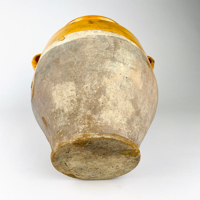 Underside of the antique 19th century French confit pot, showing the unglazed terracotta foot with dense age-related abrasion, dark marks, clay variation and small remnants of yellow glaze around the edge. No maker's stamp is visible on the base, supporting the utilitarian handmade character of this old French pottery vessel and its authentic rustic surface.