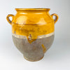 Antique French terracotta confit pot from the 19th century, with a lustrous yellow ochre glazed upper section set against the unglazed pale grey-beige lower body. Twin loop handles, a flared lip and a pronounced taper toward the foot give the vessel a sculptural silhouette, while chips, scratches and glaze variation preserve its aged French country decor appeal.