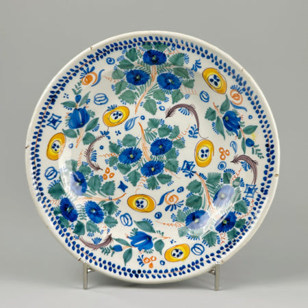 Antique Spanish Manises plate with vibrant floral design in blue, green, yellow, and orange, hand-painted on tin-glazed ceramic surface, shown from above with decorative border and wide diameter perfect for wall display.