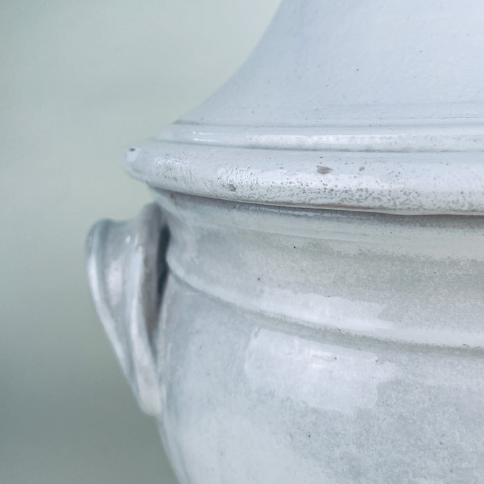 French white ceramic decorative bowl in a traditional pedestal tureen form, with a deep rounded body, fitted lid, mushroom shaped knob, and two applied loop handles. The mottled white glaze reveals traces of warm terracotta beneath, creating a timeworn surface suited to wabi sabi decor and rustic home decor.