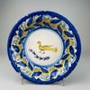 Antique Spanish Manises ceramic plate with hand-painted yellow bird, polychrome floral border, and scalloped blue rim, photographed upright to highlight its 27 cm width and folk art style for rustic Mediterranean wall decor or collector display.