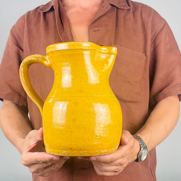 Antique Spanish pottery jug from La Rioja with a warm mustard-yellow surface, gently swelling body and high curved handle attached beneath the rim and along the shoulder. Historic rubbing along the handle and scattered exposed-clay patches contrast with the glossy glaze, giving the substantial pitcher an authentic aged finish for rustic and Mediterranean interiors.