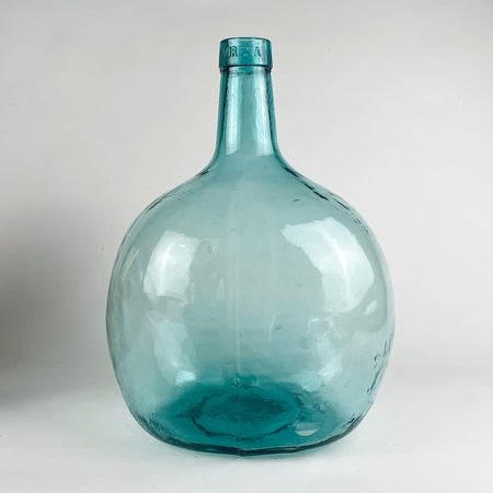 This vintage Spanish demijohn is made in hand blown blue green glass and bears the Viresa name embossed at the neck. Its broad rounded form and narrow collar identify it as a wine carboy bottle originally used for liquid storage, now ideal as a large decorative vase for olive branches in Mediterranean decor or rustic home decor.