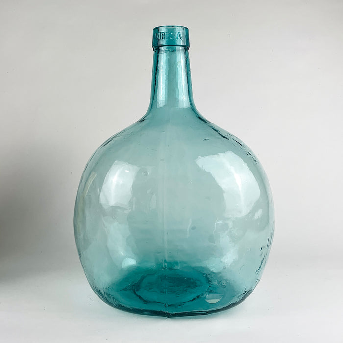 This vintage Spanish demijohn is made in hand blown blue green glass and bears the Viresa name embossed at the neck. Its broad rounded form and narrow collar identify it as a wine carboy bottle originally used for liquid storage, now ideal as a large decorative vase for olive branches in Mediterranean decor or rustic home decor.
