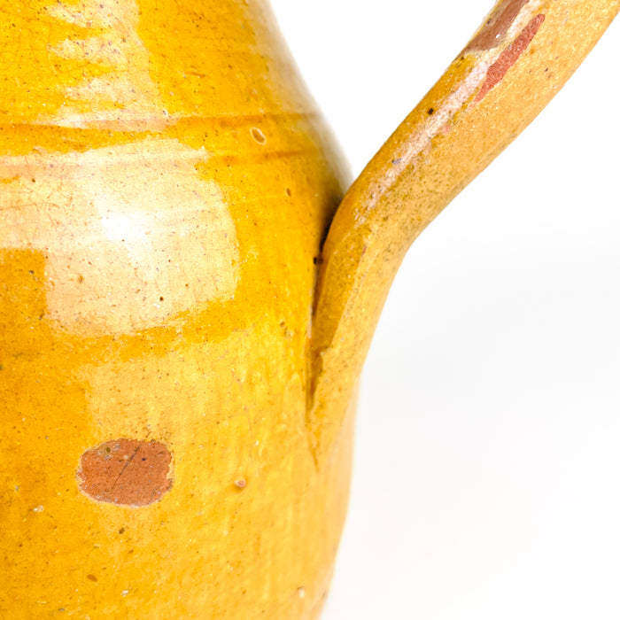 Antique yellow pottery jug sourced in La Rioja, measuring 22 cm high with an equal 22 cm span from the pouring spout to the handle. Its sturdy wheel-thrown construction, warm ochre colour, shaped mouth and elongated handle create a strong sculptural silhouette suited to rustic kitchen shelving, farmhouse decor and collected Spanish folk pottery.