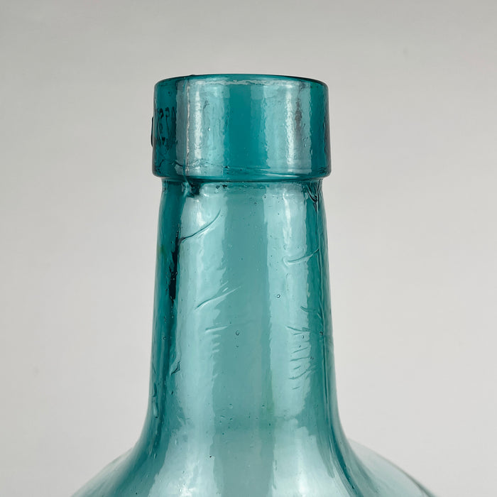 Large vintage Viresa bottle in hand blown blue green glass, made in Spain and shaped as a demijohn with broad rounded body and upright neck. The surface shows small age marks, internal bubbles, and slight optical distortion typical of handmade glass. It can be used as a floor bottle, bottle vase, or decorative vessel in coastal decor.