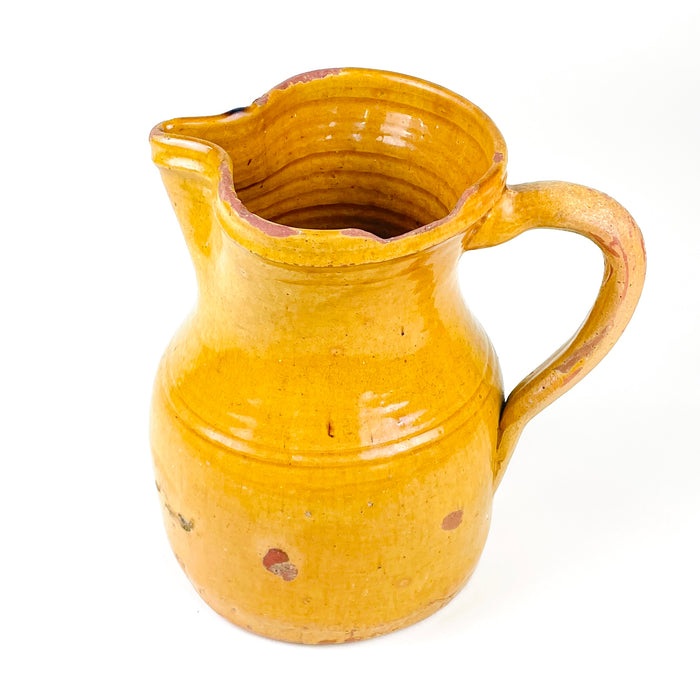 Antique yellow pottery jug sourced in La Rioja, measuring 22 cm high with an equal 22 cm span from the pouring spout to the handle. Its sturdy wheel-thrown construction, warm ochre colour, shaped mouth and elongated handle create a strong sculptural silhouette suited to rustic kitchen shelving, farmhouse decor and collected Spanish folk pottery.