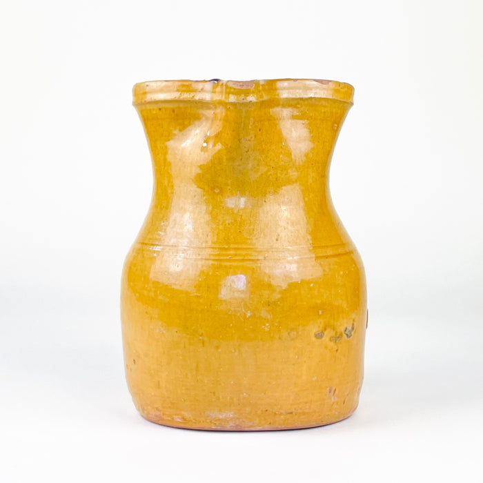 Spanish folk pottery pitcher from La Rioja with a glossy yellow glaze, broad rounded proportions and a tall applied handle. The 19th century jug retains authentic chips, glaze losses, surface rubbing and exposed terracotta around the rim and body, creating a naturally timeworn appearance suited to farmhouse decor, rustic shelving and pottery collections.