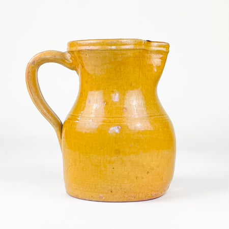 Antique Spanish yellow terracotta jug from La Rioja with a substantial wheel-thrown body, gently rounded shoulder, narrowed neck, shaped pouring spout and long applied strap handle. The rich ochre glaze, exposed red clay, turning lines and authentic surface wear give this late 19th century pottery pitcher a distinctive folk character for Mediterranean and farmhouse decor.
