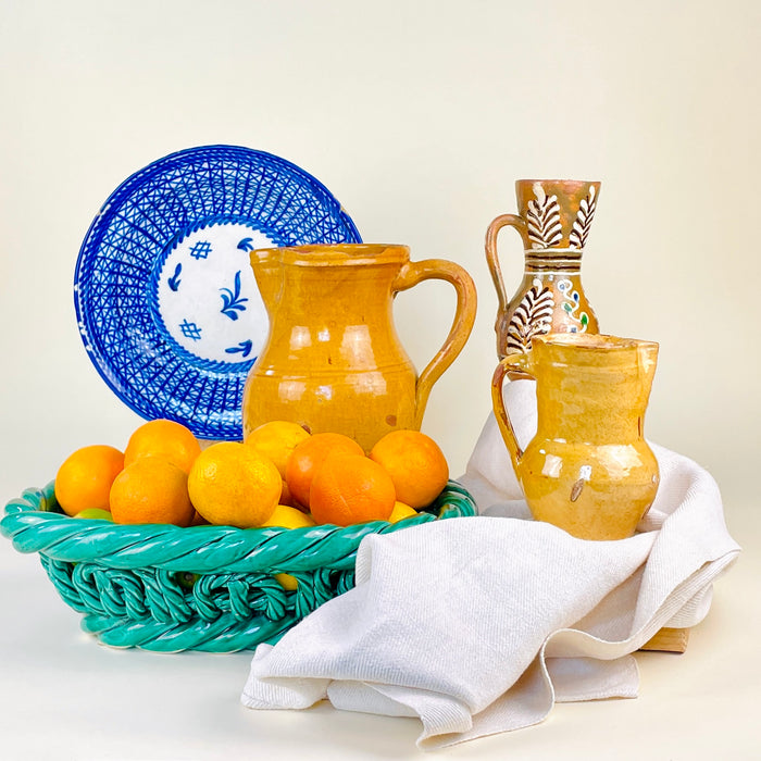 Spanish yellow earthenware jug from La Rioja with a softly rounded body, constricted neck, flared rim and curved strap handle. The surface retains a glossy honey glaze with areas of rubbing, exposed terracotta and natural firing variation, giving the antique vessel a warm sculptural presence for rustic home decor and pottery collections.