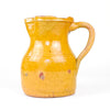 Late 19th century glazed earthenware pitcher from La Rioja, formed with a broad cylindrical lower body, softly curved shoulder, pinched pouring lip and tall looping handle. The luminous honey-yellow glaze varies naturally across the handmade surface, revealing scattered terracotta patches, historic wear and subtle kiln marks associated with traditional Spanish pottery.