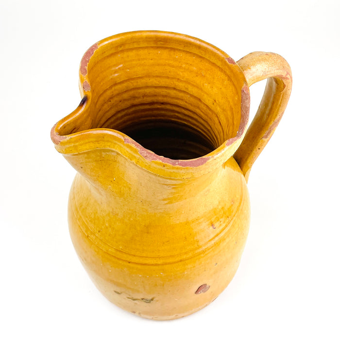 Antique Spanish terracotta jug from La Rioja with a broad mouth, pronounced pouring spout and elongated handle that follows the curve of the vessel. The ochre glaze has softened through age, revealing red clay along the handle, rim and lower body and creating a richly patinated surface for Mediterranean decor or collected folk pottery.