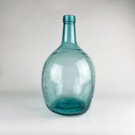 Large Viresa demijohn in blue glass from Spain, made in hand blown utility glass with a substantial rounded body, tapered neck, and visible irregular bubbles suspended in the glass. This vintage bottle works as a sculptural floor vase, statement table centerpiece, or oversized bottle decor in coastal decor and vintage home decor settings.
