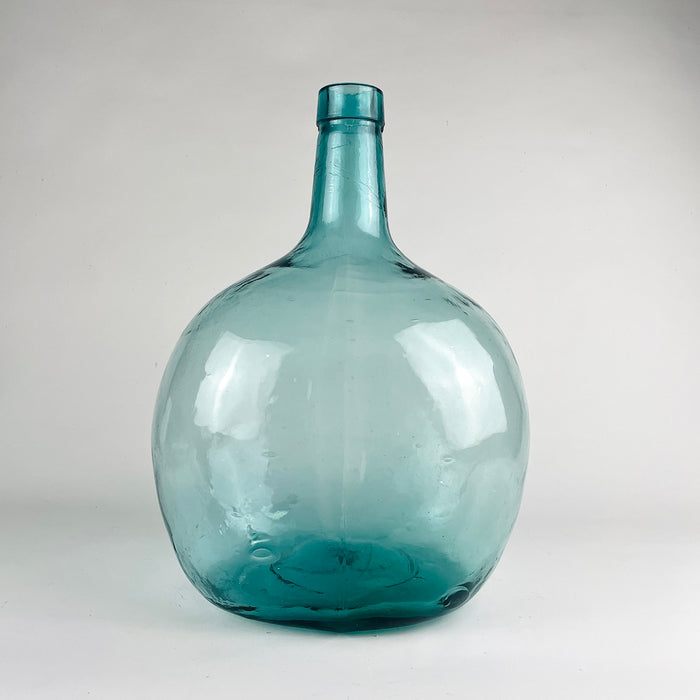 Large Viresa demijohn in blue glass from Spain, made in hand blown utility glass with a substantial rounded body, tapered neck, and visible irregular bubbles suspended in the glass. This vintage bottle works as a sculptural floor vase, statement table centerpiece, or oversized bottle decor in coastal decor and vintage home decor settings.