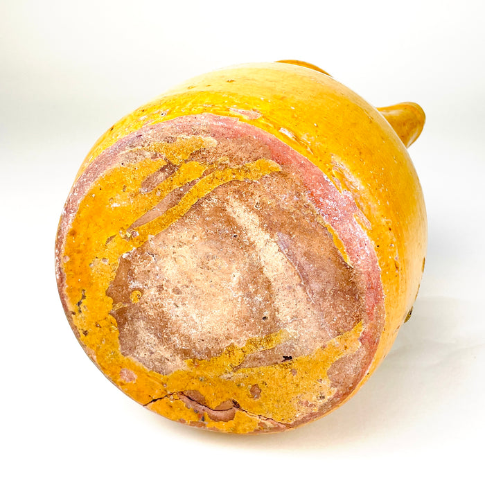 Antique wine or water jug from La Rioja with a rich golden-yellow glaze and substantial 1.4 kg earthenware construction. The tall handle, shaped lip and broad lower body create a practical pouring form, while visible wheel rings, kiln marks and aged glaze losses contribute to the authentic folk character of this 19th century Spanish pitcher.