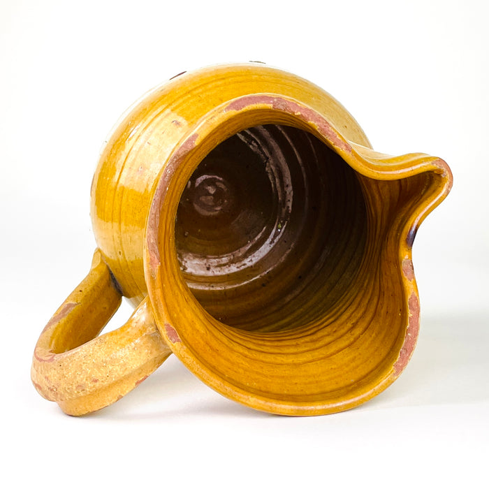 Yellow glazed pottery pitcher from La Rioja with a rounded wheel-thrown body and gently flared neck. Historic glaze wear exposes the terracotta beneath in scattered circular patches, while fine craquelure and subtle surface irregularities give the antique jug an expressive handmade finish for farmhouse kitchens, console displays and rustic interiors.